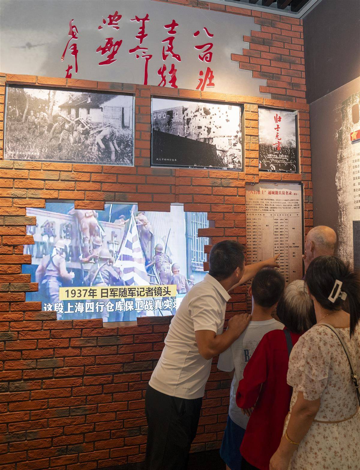 胡志全（左一）和家人在八百壮士史料展板上寻找爷爷胡梦生的名字.jpg